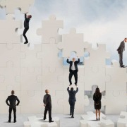 Bild auf dem mehrere Geschäftsleute versuchen ein riesiges Puzzle zusammen zu bauen.