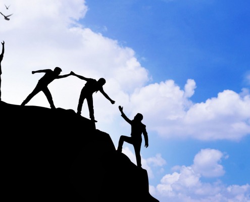 Personen auf einem Gipfel, wie sie sich gegenseitig helfen